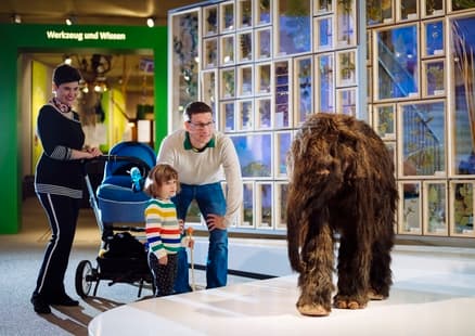 Familie mit Kinderwagen bestaunt Mammut Nachbildung