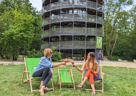 Erwachsene auf Liegestühlen mit Cocktail aus Gastronomie vor Erlebnisturm Höhlenblick