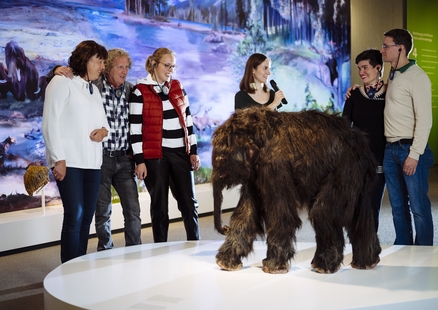 Erwachsene lauschen mit Kopfhörern einer Führung neben Mammut