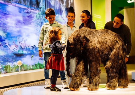 Kind steht mit Familie neben Baby Mammut in Ausstellung