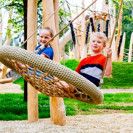 Kinder sitzen in Nestschaukel auf Steinzeitspielplatz in Outdoor Erlebniswelt