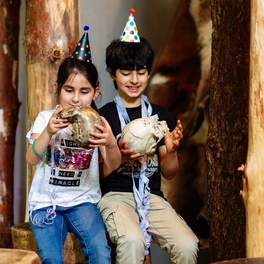 Kinder mit Partyhut untersuchen Schädel bei Steinzeitgeburtstag im Museum