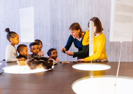 Mitarbeiterin erklärt Kindern etwas bei Führung in Aussstellung