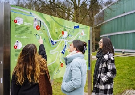 Erwachsene zeigen vor Museum auf Übersichtskarte der Outdoor Erlebniswelt