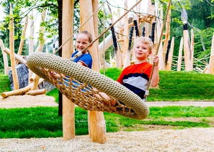 Kinder sitzen in Nestschaukel auf Steinzeitspielplatz in Outdoor Erlebniswelt